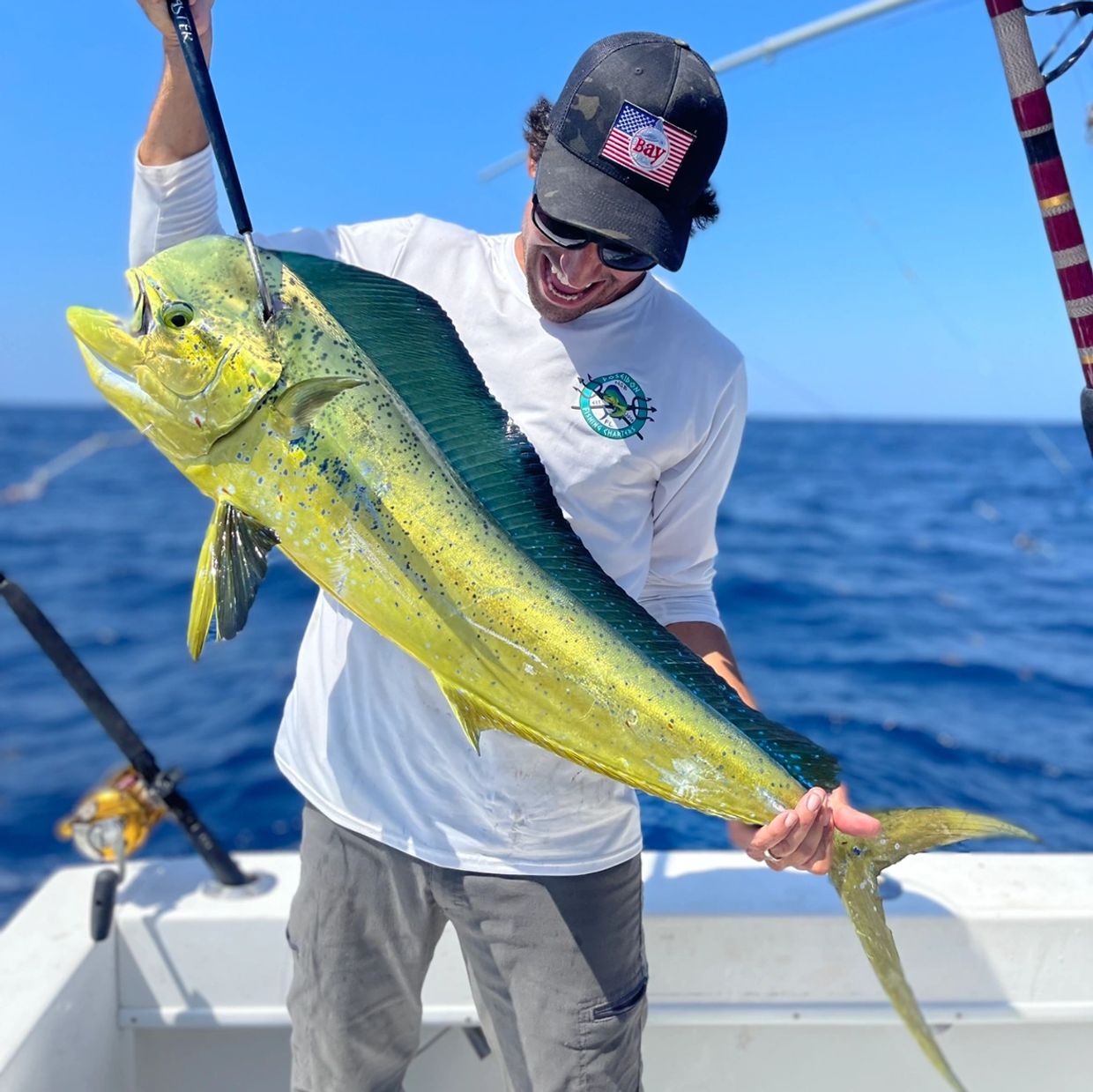 Man proudly holds a large, colorful mahi-mahi fish on a boat under clear blue skies.