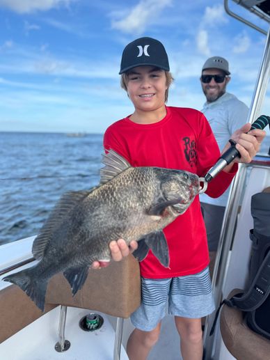 Boy proudly holding a large fish on a boat with a man smiling behind.