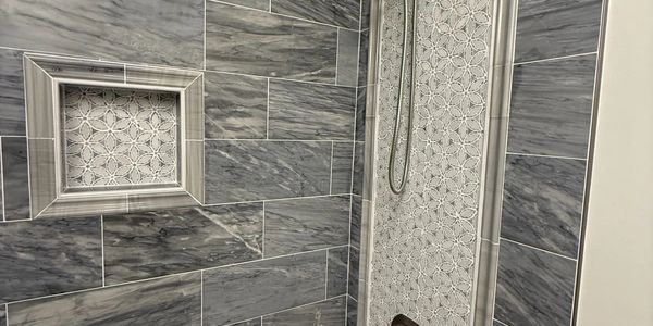 Modern bathroom shower with gray marble tiles and decorative mosaic accents.