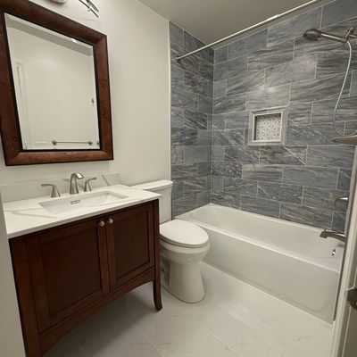 Modern bathroom with wooden vanity, white bathtub, and gray tiled shower walls.