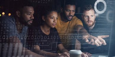 Four diverse colleagues focused on coding and data analysis at a computer.