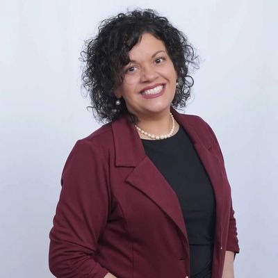 Smiling woman with curly hair in a maroon blazer.