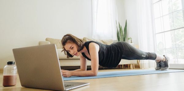 Young asian woman doing a plank in front of laptop during her 1-2-1 online coaching session.