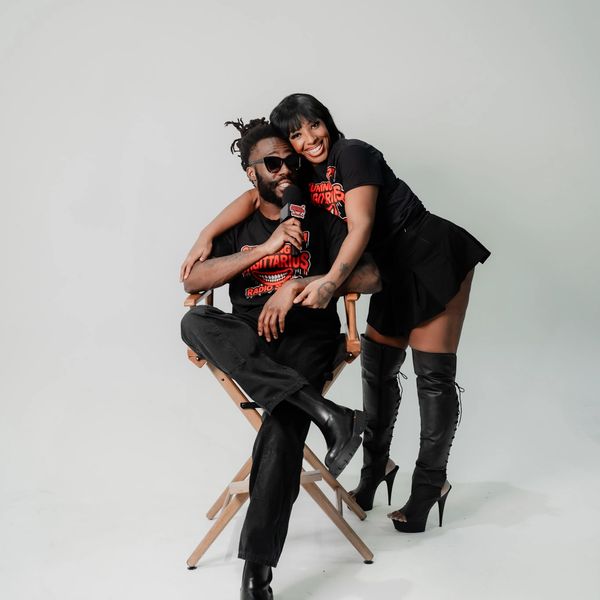 A happy couple in black outfits posing against a white backdrop.
