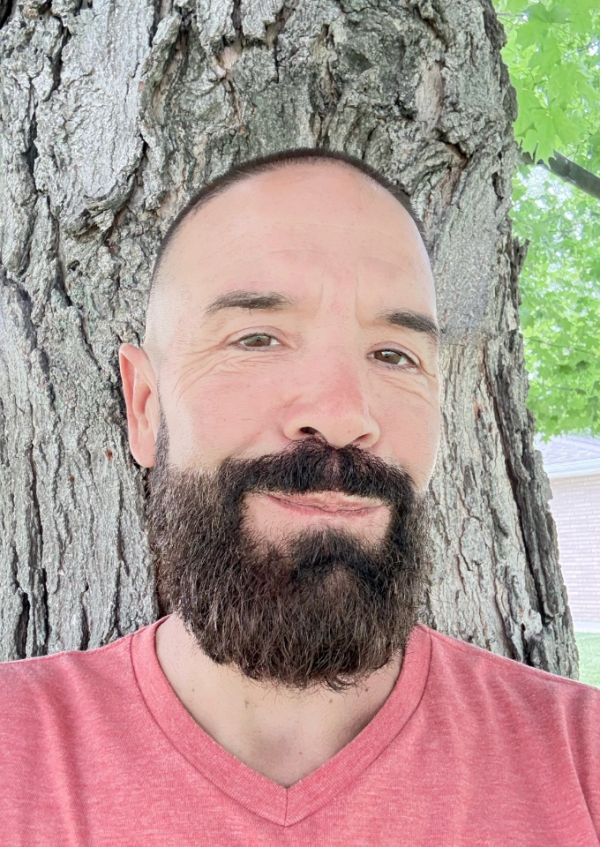 Man with a full beard and shaved head in a pink shirt.