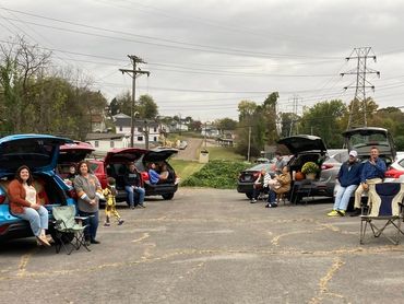 People sitting by their car trunks in an outdoor setting.