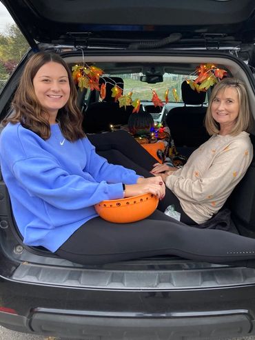 Two women sitting in a decorated car trunk with a Halloween theme.