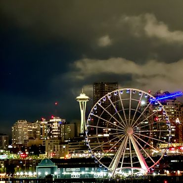 Night view of Seattle skyline with Space Needle and Ferris wheel illuminated.