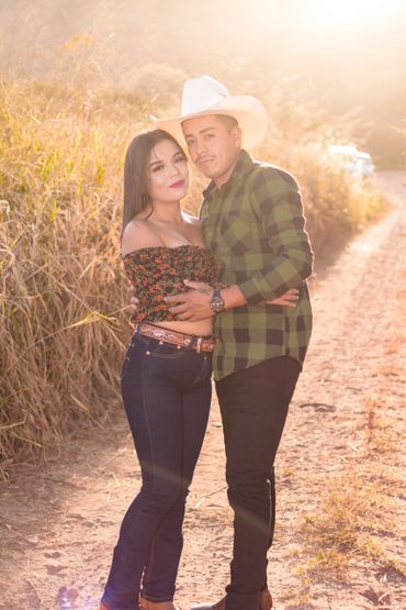 A couple embraces on a sunlit dirt path surrounded by tall grass.