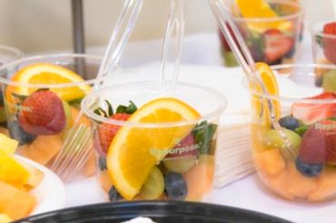 Clear cups filled with fresh fruit slices including oranges, strawberries, and grapes.