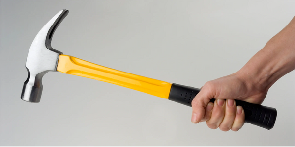 Hand holding a yellow-handled claw hammer against a plain background.