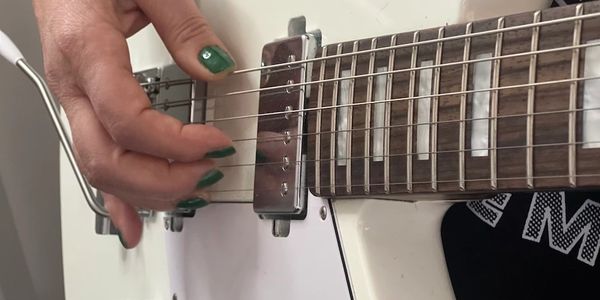 Hand with green nails playing white electric guitar strings.