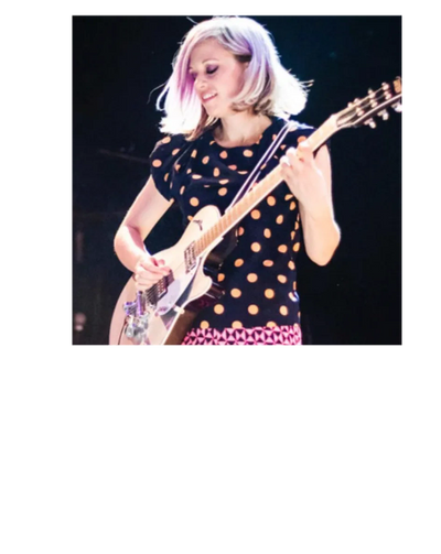 Woman playing electric guitar on stage with a joyful expression.