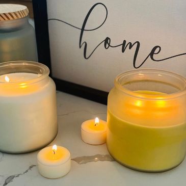 Lit candles in cozy jars on a marble surface with a 'home' sign in the background.