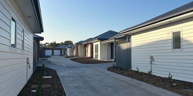 A clean concrete driveway between two rows of modern houses during daylight.