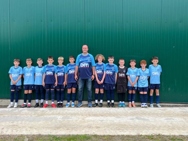 Youth soccer team posing with their coach against a green wall.