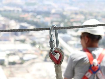 Safety carabiner locked on a cable with a worker in a harness.