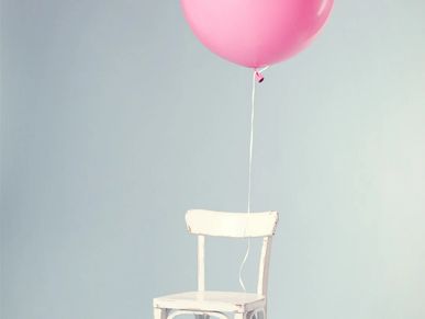 A white chair with a pink balloon attached against a pale blue wall.