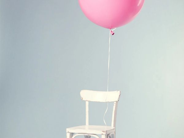 A white chair with a pink balloon attached against a pale blue wall.