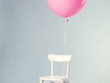 A white chair with a pink balloon attached against a pale blue wall.