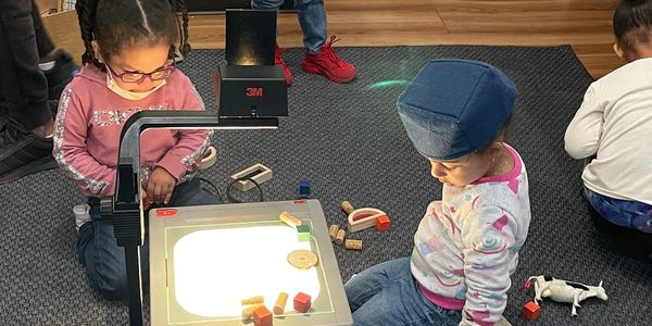 Preschoolers in the dramatic play area exploring with materials at the light projector.