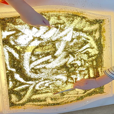 Two children playing with a tray of golden glitter.