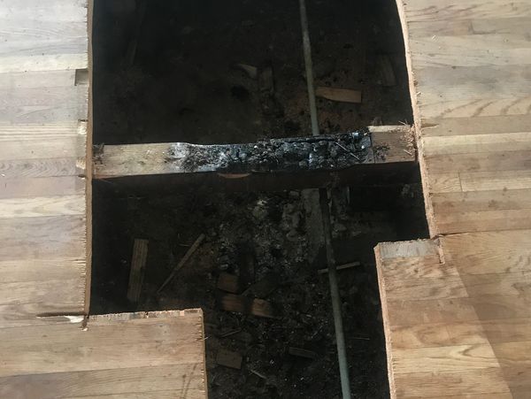 Section of wooden floor removed revealing blackened, burnt wood and debris beneath.