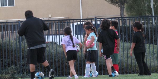 Coach instructing young children on soccer field during practice.