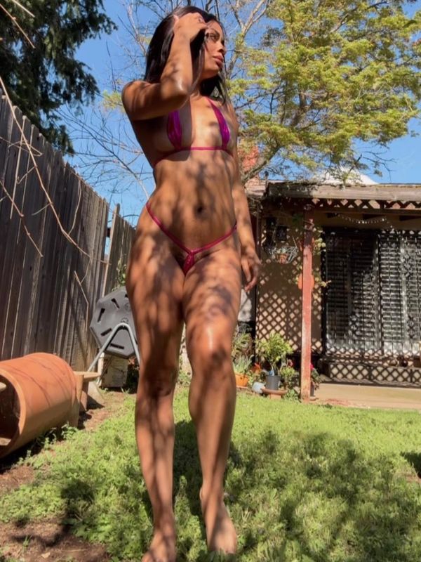 Woman in a pink bikini standing outdoors with shadows of tree branches on her body.
