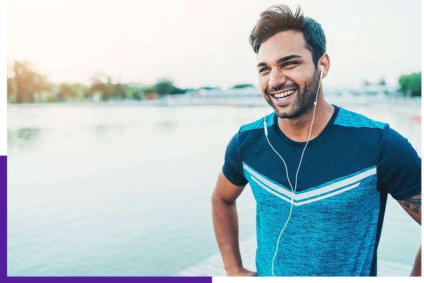 Happy young man in sporty attire with earphones by the water.