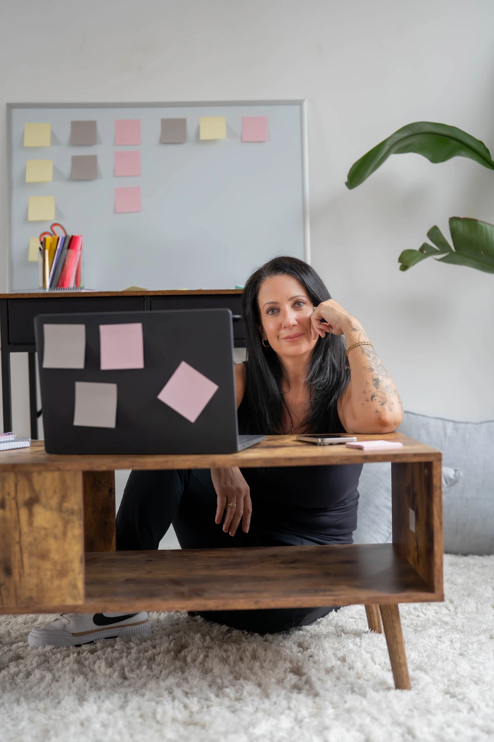 Woman sitting on the floor behind a laptop with sticky notes in a cozy workspace.