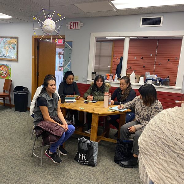 Group of women engaged in discussion around a wooden table in a cozy room.