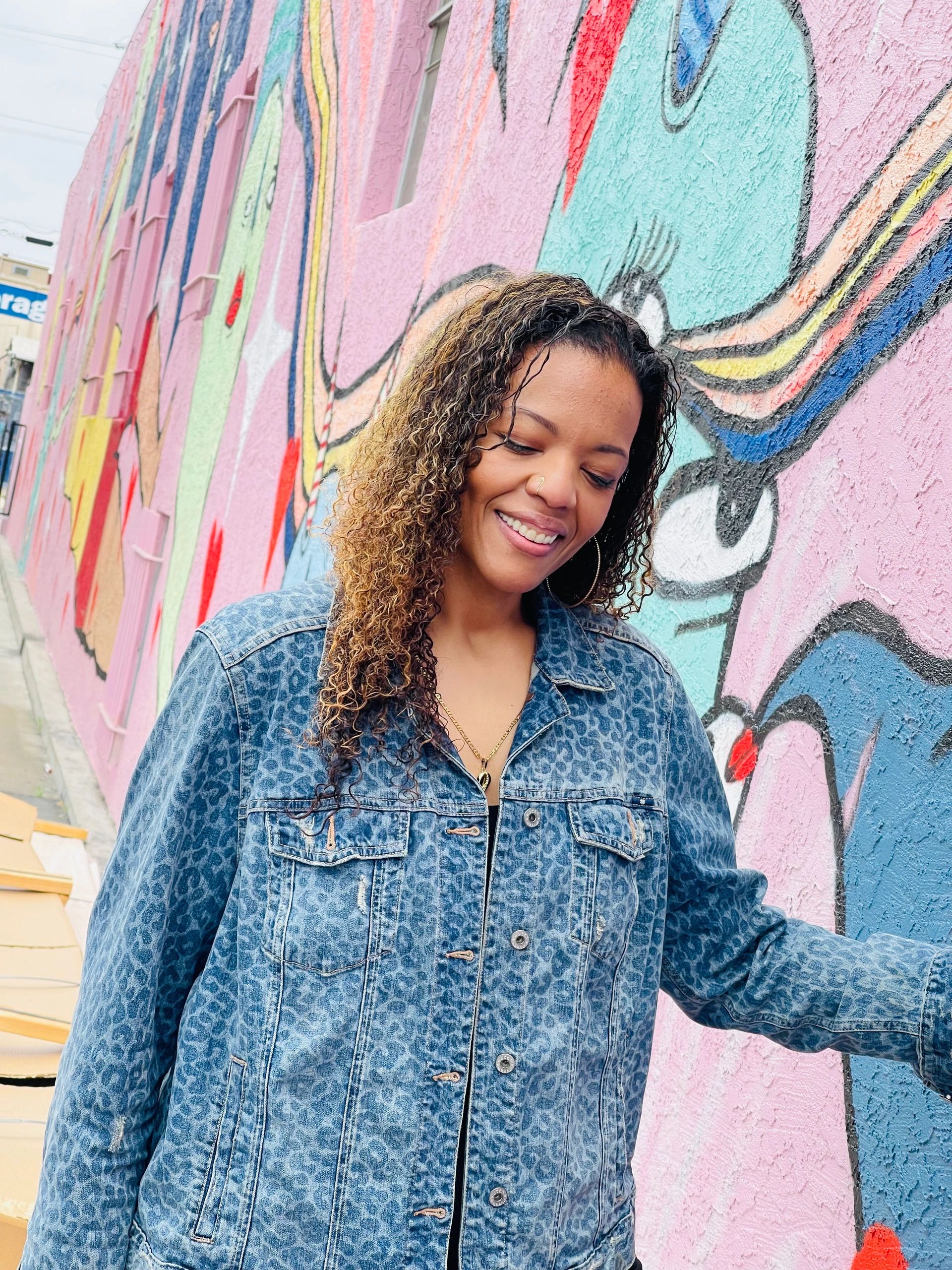 a tall brown-skinned woman with long curly hair standing in front of a brightly colored art mural