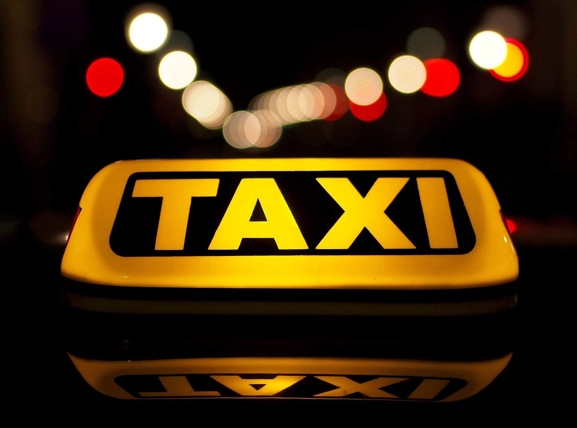 Illuminated taxi sign against blurred city lights at night.