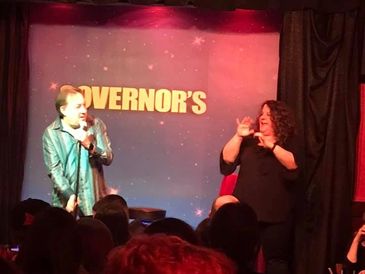 Governor’s Comedy Club stage with a comedian on the left and an interpreter on the right. 