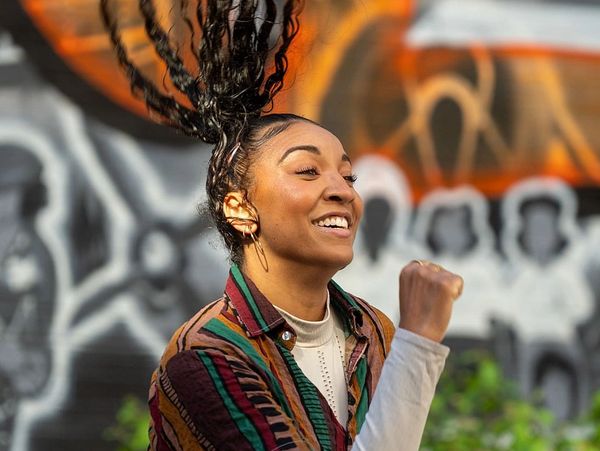 A joyful woman with braided hair flips her hair outdoors in front of graffiti.