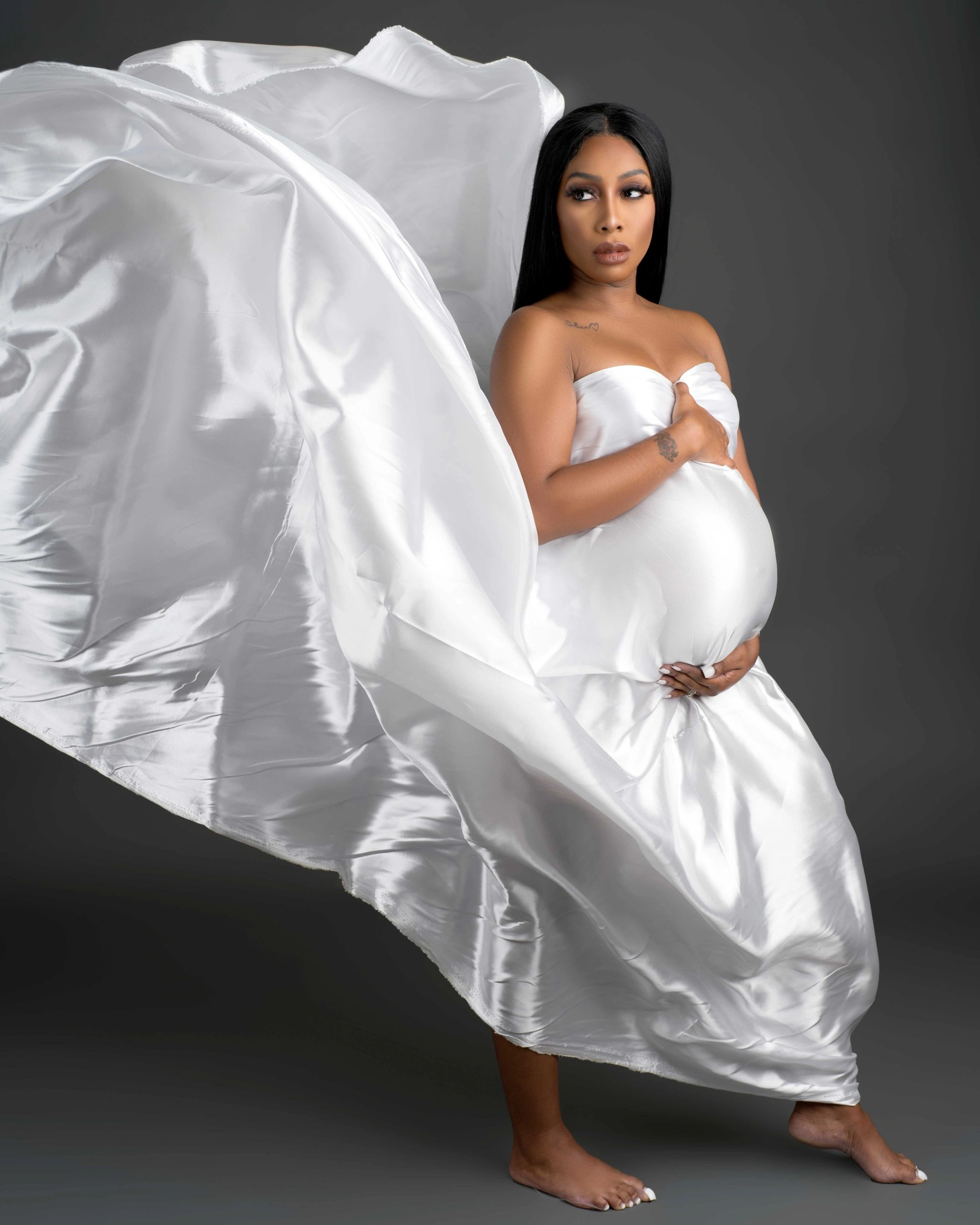 Pregnant woman in flowing white gown against dark background.