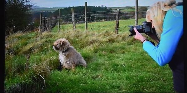 Sandie holding a camera and taking a photo of her dog in the countryside