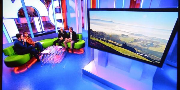 Presenters in the studio of The One Show sat on the sofa discussing a landscape image shown on a lar
