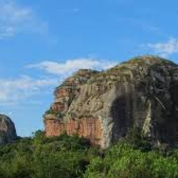 Large rocky hill with greenery under a blue sky.