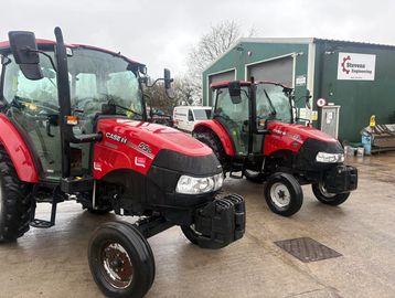 Two red tractors parked outside a green building.