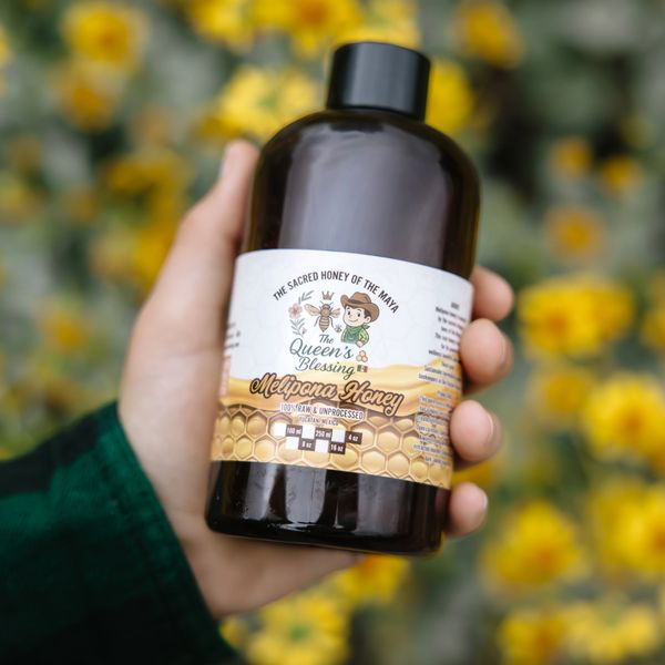 Hand holding a bottle of raw Melipona honey with yellow flowers blurred in the background.