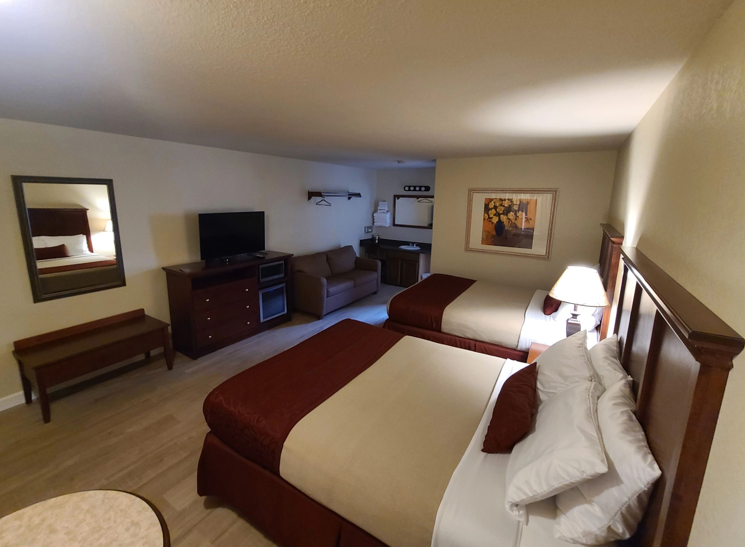 A wide view of a hotel room with two beds, a sofa, and a TV.