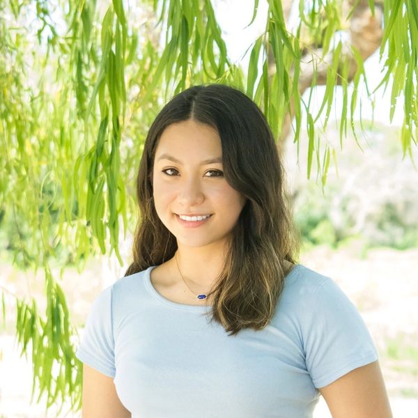 Young woman smiling under green hanging leaves.