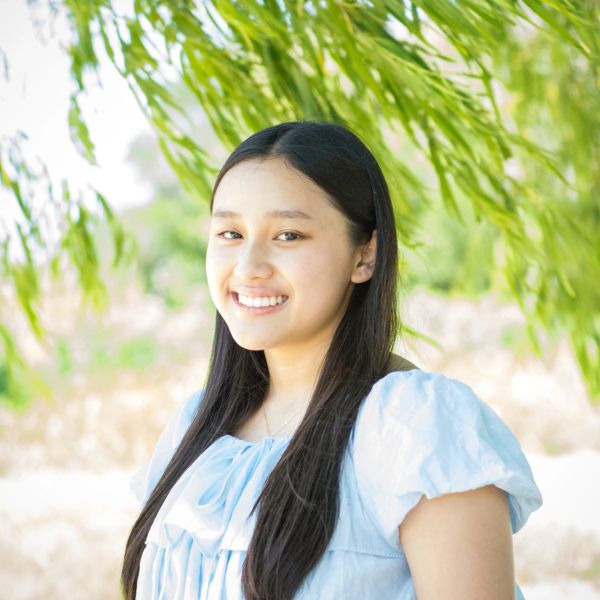 Young woman smiling under green leaves.