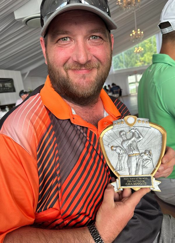 Man proudly holding a golf tournament champion trophy indoors.