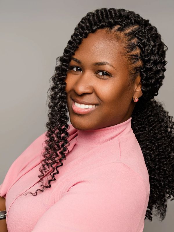 Confident woman, who is a Licensed Professional Counselor that provides mental health therapy in her private practice entitled MPowered Counseling Services LLC, smiling warmly, wearing a pink top with curly braided hair.