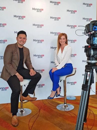 Two people sitting on stools in front of a Money 20/20 backdrop.