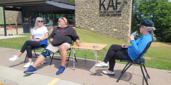 Three people sitting outdoors near a visitor center on a sunny day.