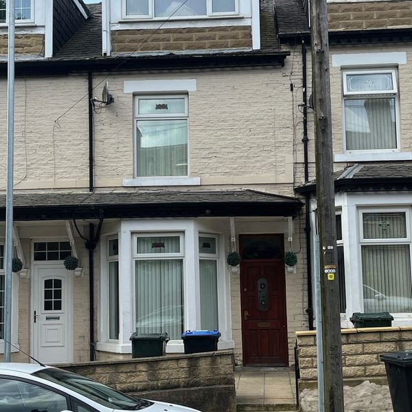Front view of a beige brick terraced house with a red door and large bay window.